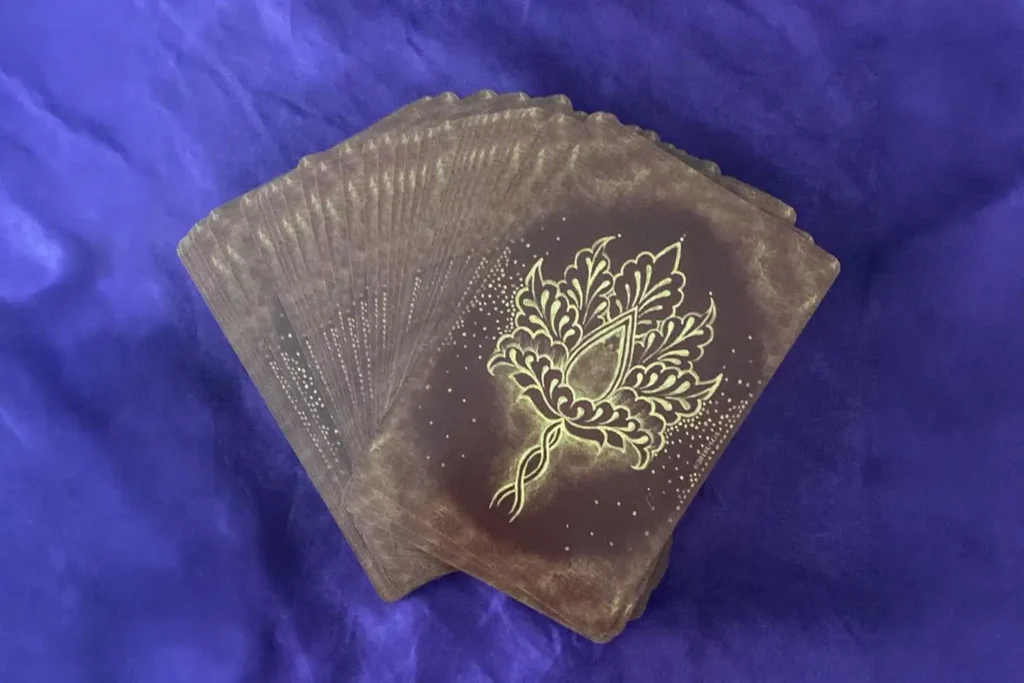 Pile of dark cards with a gold ornate floral design on the top card, placed on blue fabric.