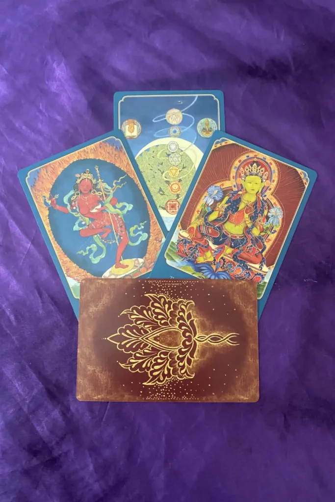 Five illustrated oracle cards arranged on purple fabric, featuring vibrant deity images with blue and red borders and a brown card with gold ornament in front.
